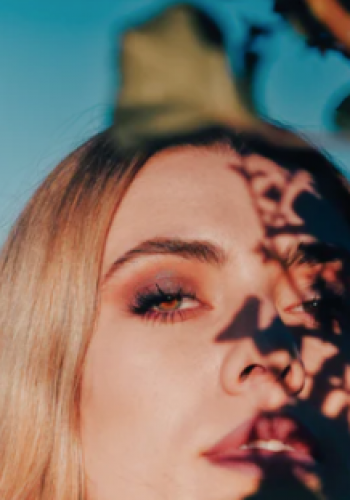 Close-up of a woman's face with shadow patterns from leaves.