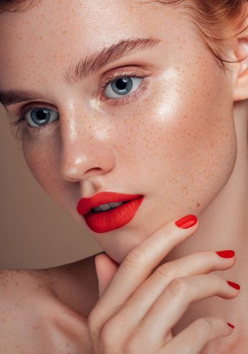 Close-up of a woman with glowing skin, red lipstick, and matching red nails.
